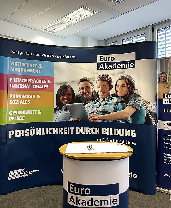 Erfolgreicher Tag der offenen Tür Infostand der Euro Akademie, mit Stehtisch, großem Roll-Up im Hintergrund