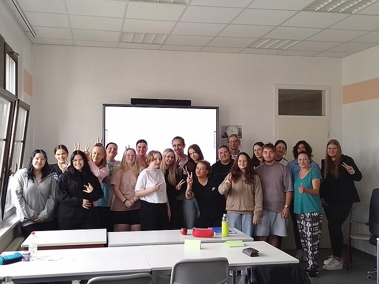 Das neue Schuljahr beginnt 21 Schüler im Klassenraum posieren lächelnd für das Klassenfoto. Einige heben ihre Finger zu Peace-Zeichen, eine Schülerin hebt den Daumen.