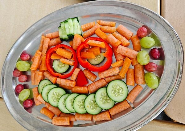 Gesund und gruselig: Kitaessen zu Halloween Auf einem silbernen Serviertablett sind verschiedene Gemüse, wie Karotten, Salatgurken und Paprika zu einem gruseligen Gesicht angerichtet.