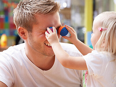 Ein Mädchen hält ihrem Kinderpfleger zwei bunte, kleine Bälle vor die Augen.
