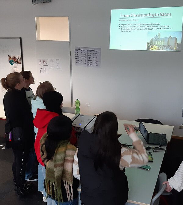 Der nächste Schritt zur Karriere: Career Week Schülerinnen stehen in einem Klassenzimmer und betrachten eine Präsentation, die an die Wand geworfen wurde, mit dem Titel "From Christianity to Islam".