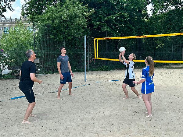 Beachvolleyball mitten in Hannover Ein Lehrer und drei Schüler*innen der Euro Akademie Hannover stehen im Kreis auf einem Beachvolleyballfeld und werfen sich gegenseitig den Volleyball zu.