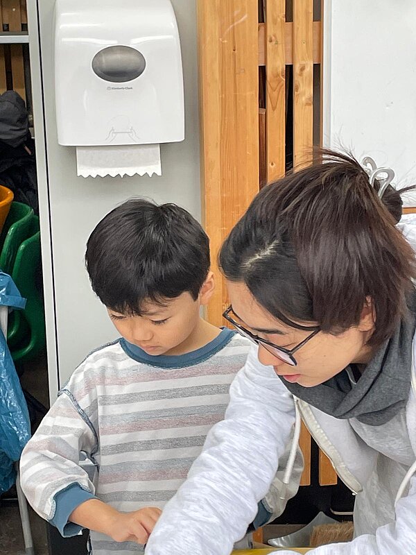 Erwachsene Person unterstützt ein Grundschulkind konzentriert bei einer Druckarbeit; Nahaufnahme am Werktisch.