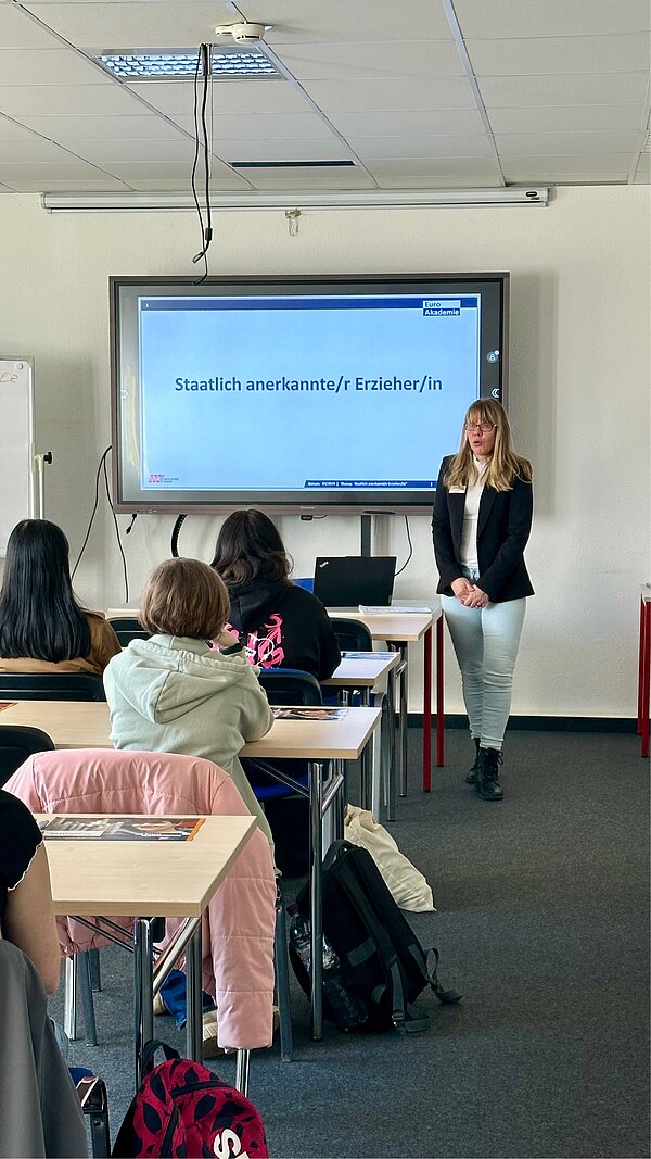 SCHAU REIN! – Woche der offenen Unternehmen Sachsen Eine Frau steht vorne im Klassenraum vor einer Präsentationsfolie mit dem Titel „Staatlich anerkannte/r Erzieher/in“, während die Teilnehmenden an Tischen sitzen und zuhören.