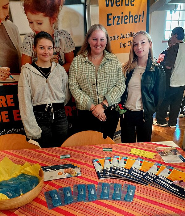 Karriere mit Herz Drei Schülerinnen posieren lächelnd am Messestand der Euro Akademie für ein Foto.