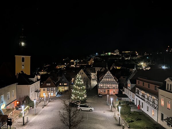 Blick über einen beleuchteten Altstadt-Marktplatz bei Nacht mit Weihnachtsbaum, Fachwerkhäusern und Kirche im Hintergrund.