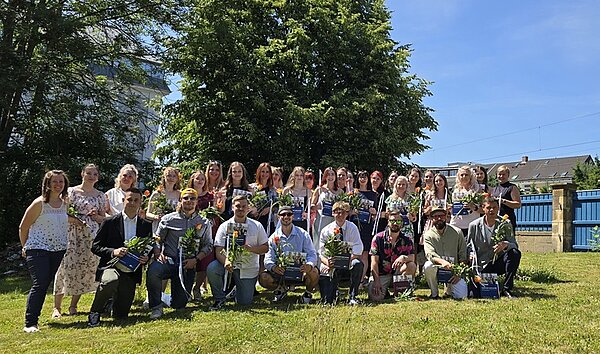Die Absolventinnen und Absolventen der Euro Akademie Hohenstein-Ernstthal posieren draußen, bei herrlichem Sommerwetter gemeinsam für ein Erinnerungsfoto.