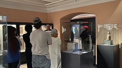 Die Auszubildenden stehen im Museum vor dem Mitarbeitenden, der ihnen Wissenswertes zur Ausstellung erzählt.