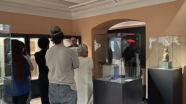 Die Auszubildenden stehen im Museum vor dem Mitarbeitenden, der ihnen Wissenswertes zur Ausstellung erzählt.
