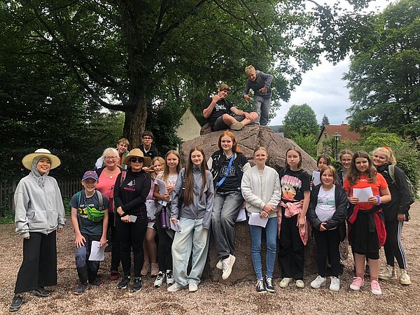 Sprachprojekte mit internationalem Flair Alle Mädchen und Jungs im Teenageralter stehen für ein Gruppenfoto nebeneinander vor einem Baum und lächeln in die Kamera.