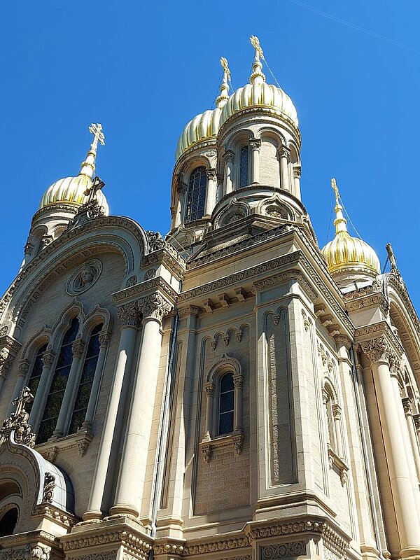 Detailansicht einer prächtigen historischen Kirche oder Kathedrale mit goldenen Kuppeln und aufwendigen Ornamenten vor einem klaren blauen Himmel.