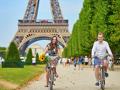Zwei Personen radeln vor dem Eiffelturm in Paris.