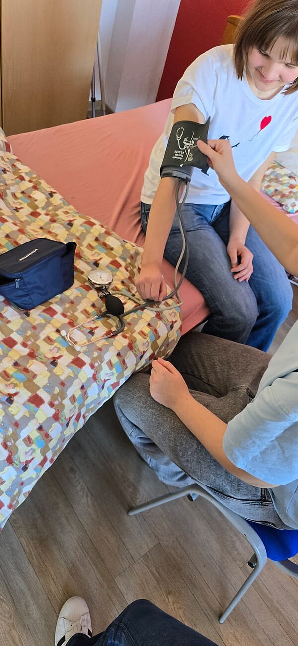 Eine Schülerin übt die Blutdruckmessung mit Manschette und Stethoskop in einer praxisnahen Lernsituation.