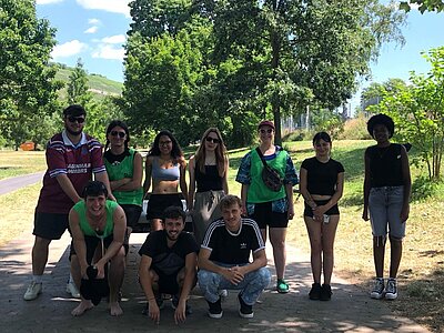 Eine Gruppe von Personen posiert für ein Foto in einem Park. Einige tragen grüne Westen und lächeln in die Kamera.