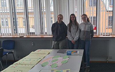 Drei weibliche Auszubildende stehen im Unterrichtsraum an der Fensterfront und posieren gut gelaunt für ein Foto.