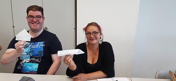 „Die Neuen“ sind da – Euro Akademie Mainz begrüßt neue Klasse der Fremdsprachenkorrespondenten Zwei Personen sitzen nebeneinander und präsentieren lachend ihre gebastelten Origami-Figuren aus Papier.