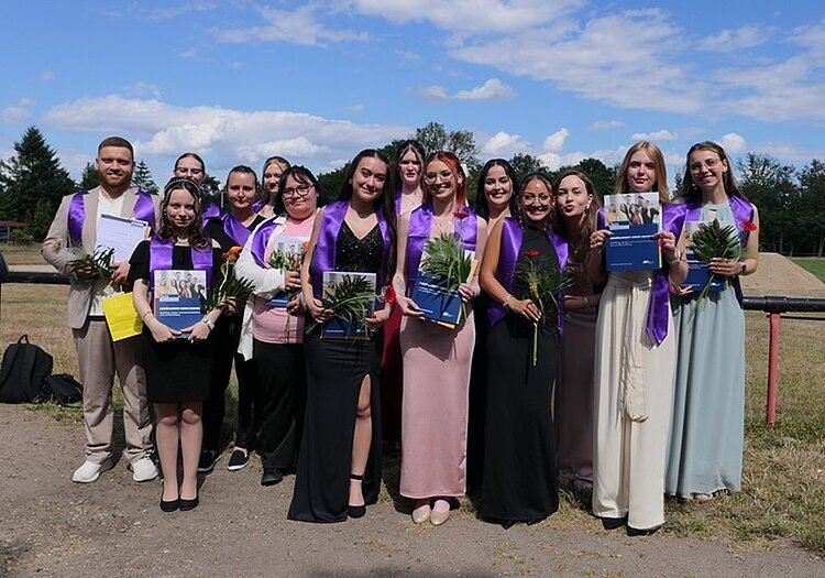 Zeugnisausgabe für die Abschlussklassen der Euro Akademie Dessau Absolventinnen und Absolventen stehen draußen und bei strahlendem Wetter für ein Gruppenfoto zusammen. Alle tragen schöne Kleidung bzw. festliche Kleider.