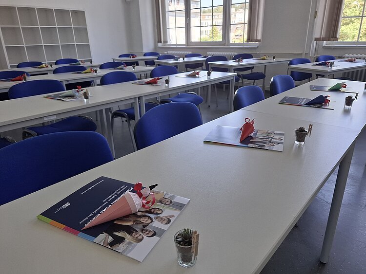 Das leere Klassenzimmer erwartet die neuen Auszubildenden: Willkommensmappen, Mini-Schultüten und eine kleine Pflanze stehen an jedem Sitzplatz bereit. Der Raum macht einen hellen und freundlichen Eindruck.