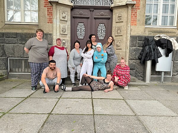 Schüler*innen posieren in Schlafkleidung und Kostümen vor dem Eingang eines historischen Schulgebäudes.