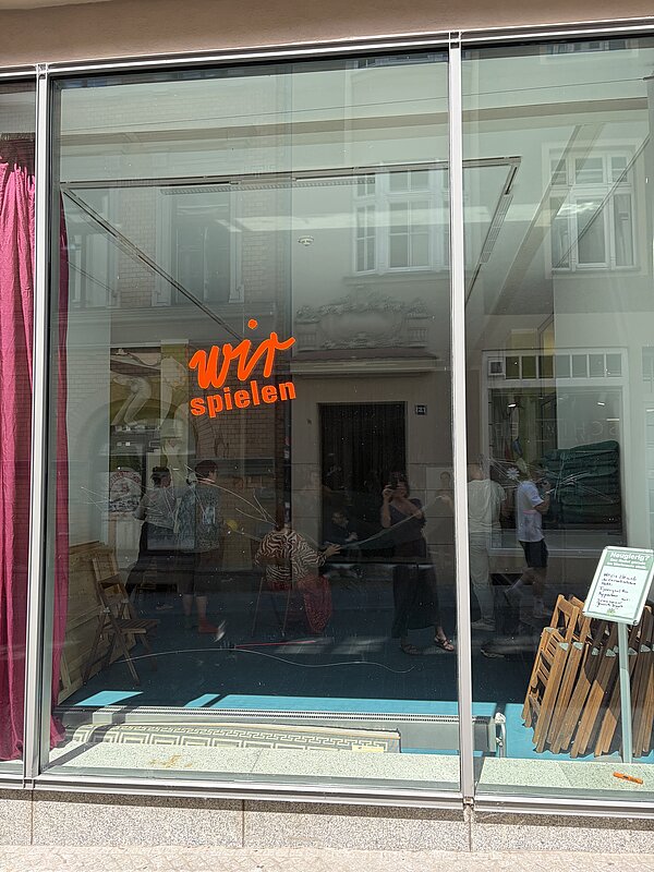 Auf einem leeren Schaufenster steht in roter Schrift: wir spielen.