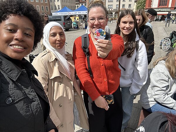 Protesttag zur Gleichstellung von Menschen mit Behinderung: Buttons für Inklusion Vier Schülerinnen stehen auf dem Würzburger Marktplatz und grinsen in die Kamera. Ein Mädchen hält einen Button in der Hand, auf dem steht: Ready for next level of humanity.