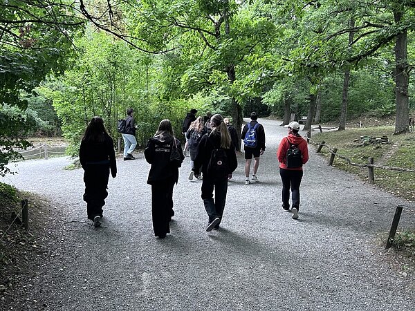 Die Auszubildenden wandern durch den Wildpark, die meisten tragen einen Rucksack auf dem Rücken.