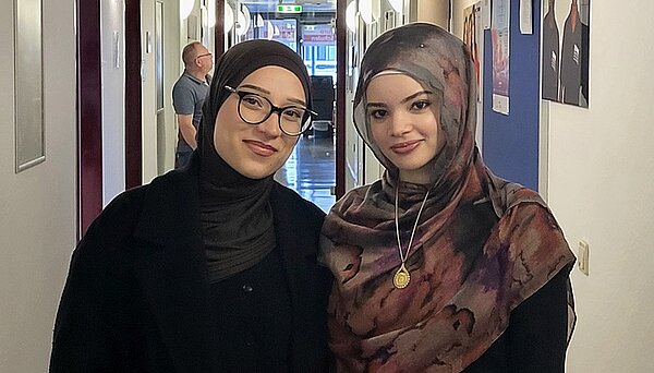 Erasmus-Speed-Dating Zwei Schülerinnen der Euro Akademie Hannover posieren gemeinsam und lächelnd für ein Foto. Eine Schülerin trägt eine Brille, die andere eine goldene Halskette und beide tragen ein Kopftuch.