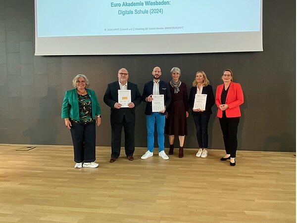 Schulleiterinnen und Schulleiter posieren mit der Urkunde in der Hand für ein Gruppenfoto.