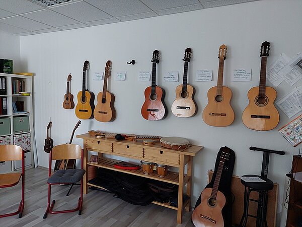 Musikraum mit vielen Akustikgitarren, die an der Wand hängen, Tamborinen und Xylophonen mit Schlegel.