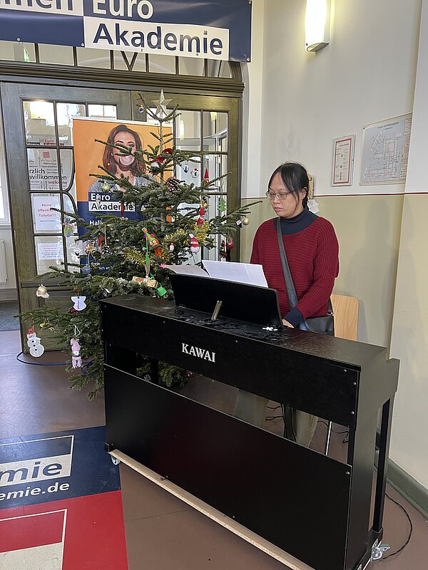 Im weihnachtlich geschmückten Eingangsbereich der Euro Akademie spielt eine Person an einem schwarzen E-Piano vor einem Weihnachtsbaum und einem Roll-up.