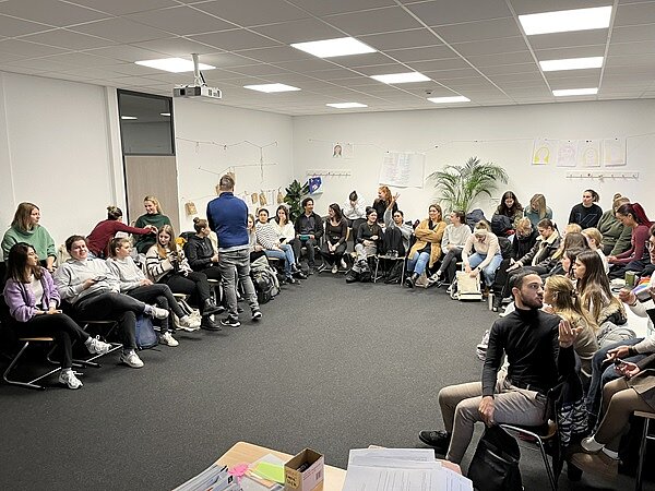 Facharbeitstag in Würzburg Alle Auszubildenden sind im großen Raum versammelt, sitzen mit ihren Stühlen an den Wänden, sodass in der Mitte Raum entsteht.