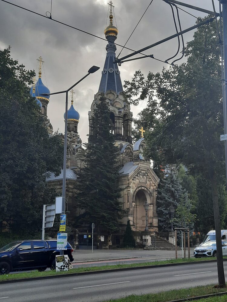 Ethikunterricht mal anders Straßenszene mit Blick auf eine orthodoxe Kirche mit blauen und goldenen Zwiebeltürmen, umgeben von Bäumen. Im Vordergrund sind Autos auf einer mehrspurigen Straße sowie Straßenlaternen und Oberleitungen zu sehen.