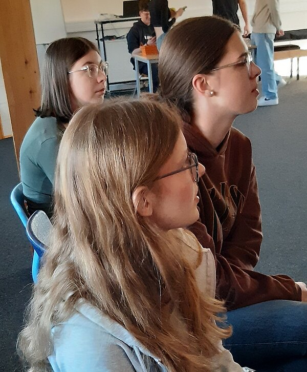 Einstimmung auf Ostern Drei weibliche Auszubildende, zwei mit braunen, eine mit blonden, langen Haaren und alle mit Brille sitzen auf Stühlen und schauen nach vor.