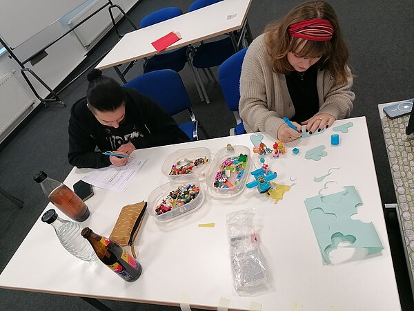 MeKoSax-Projekt „Trickfilmproduktion“ Auf einem Tisch liegen verschiedenfarbige Bögen Papier, Kinderspielzeug aus Plastik und Buntstifte. Mit Scheren Schneiden Schülerinnen und Schüler Formen aus.