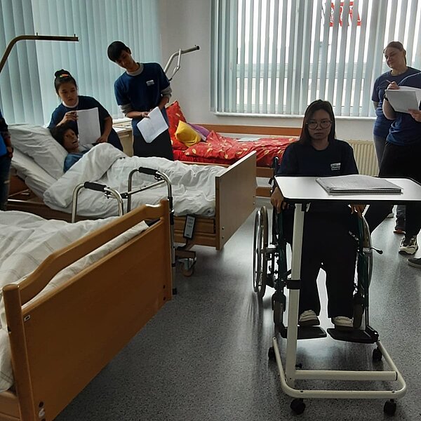 Praxisstunde an der Euro Akademie Bitterfeld-Wolfen Blick in ein Übungskrankenzimmer an der Euro Akademie Bitterfeld-Wolfen, in dem die Schülerinnen und Schüler ihre Praxisübungen durchführen. Man sieht Krankenbetten mit Aufrichthilfen, eine Auszubildende sitzt im Rollstuhl.