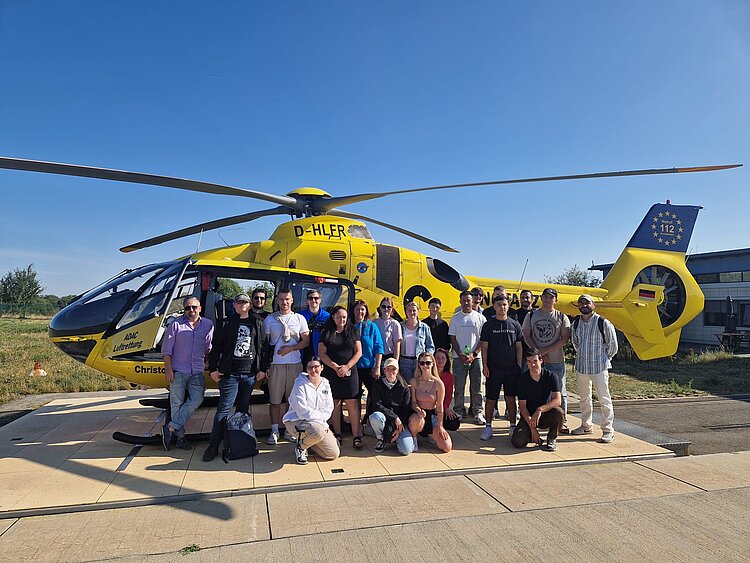 Ein unvergesslicher Tag für die Klasse der Pflegefachmänner*frauen 2022 Ein Gruppe junger Männer und Frauen steht vor einem gelben ADAC Helicopter mit der Nummer Christoph 70. Dabei ist strahlender Sonnenschein.