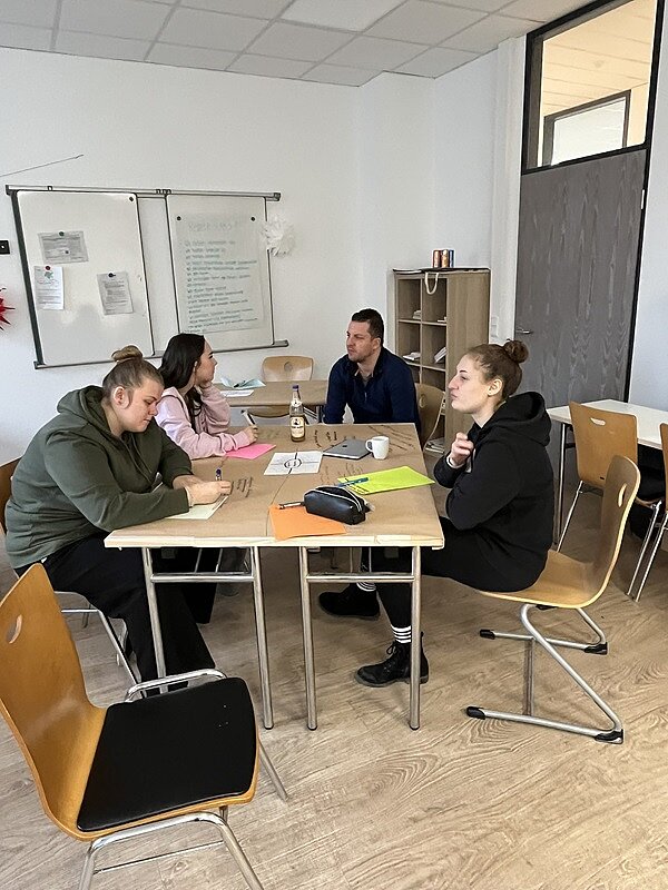 Facharbeitstag in Würzburg Vier Auszubildende sitzen an einem Tisch gegenüber und arbeiten an ihren Aufgaben.