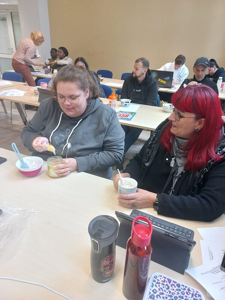 Zwei junge Frauen sitzen an einem Holztisch und essen ein Müsli.
