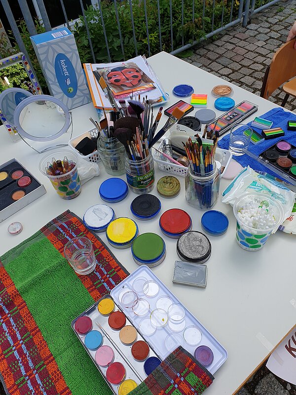 Ein erlebnisreicher Vormittag voller Spiel, Kreativität und Gemeinschaft Nahaufnahme eines Tisches mit bunten Farben, Pinseln und Schminkutensilien für Kinderschminken.