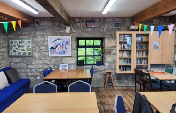 Tische mit Stühlen und im Hintergrund ein Glasschrank mit Gläsern ist zu sehen. Dabei handelt es sich um einen Raum des Galway Language Center.