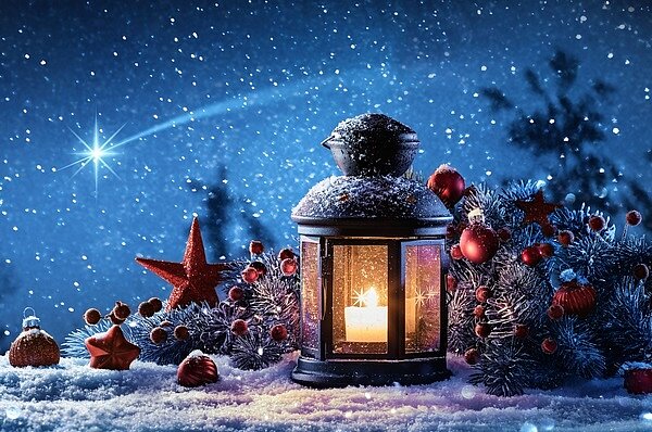 Lampe mit brennender Kerze auf Schnee, zwischen Tannenzweigen und Christbaumkugeln mit Sternschnuppe am Himmel.