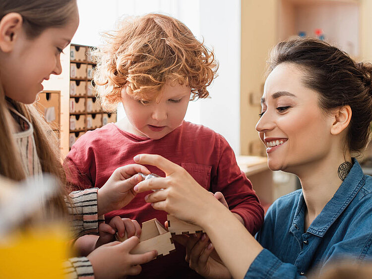 Junge Frau hilft zwei Kindern mit Bauklötzchen.