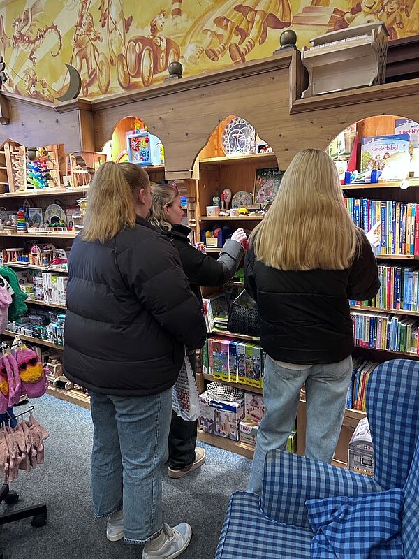 Zwei Personen stehen in einem Spielzeugladen und betrachten die Regale mit Spielzeug und Büchern.