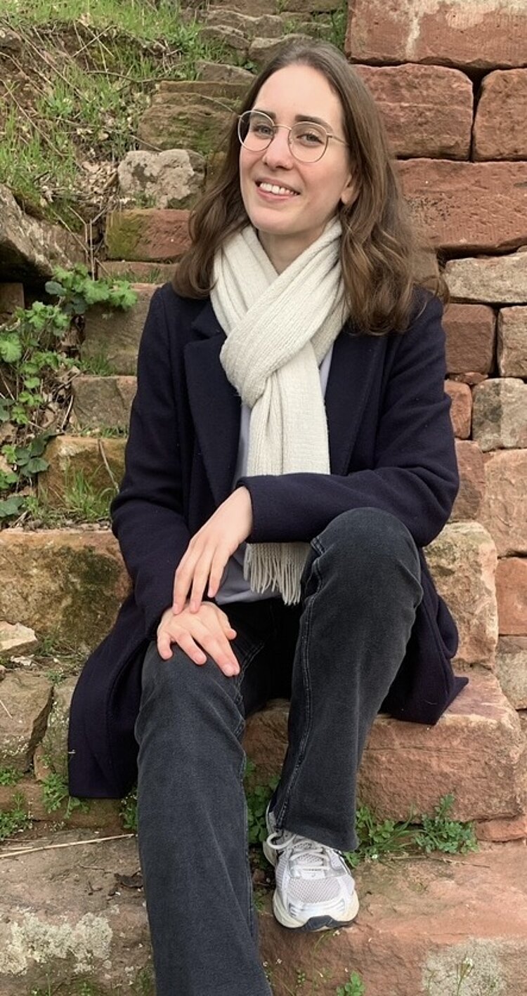 Alumni im Gespräch: Interview mit Janina Rohleder Absolventin Janina Rohleder sitzt auf einer Steintreppe und posiert lächelnd für ein Foto.