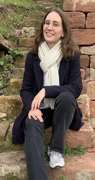 Absolventin Janina Rohleder sitzt auf einer Steintreppe und posiert lächelnd für ein Foto.