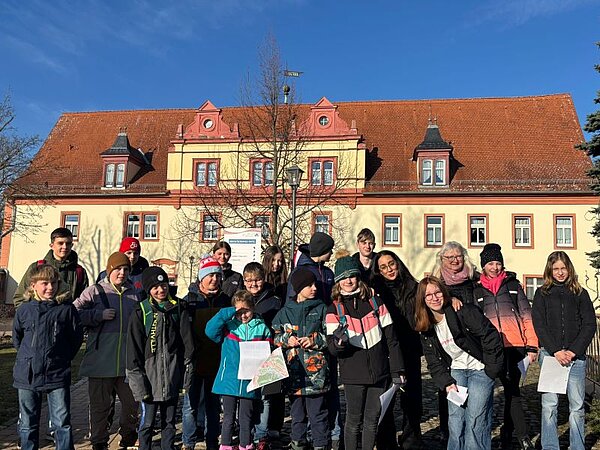 Winter-Sprachferien 2025: „Living in Fairy Tales“ Eine Gruppe mit Schülern und einer Lehrkraft in winterlicher Kleidung hat sich für ein Foto vor einem historischen Gebäude aufgestellt. Die Sonne scheint und der Himmel ist blau.