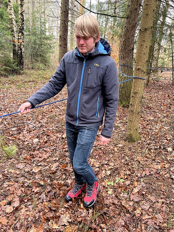 Ein Schüler hält sich an einem blauen Seil fest und läuft mit geschlossenen Augen von einem Baum zum nächsten.