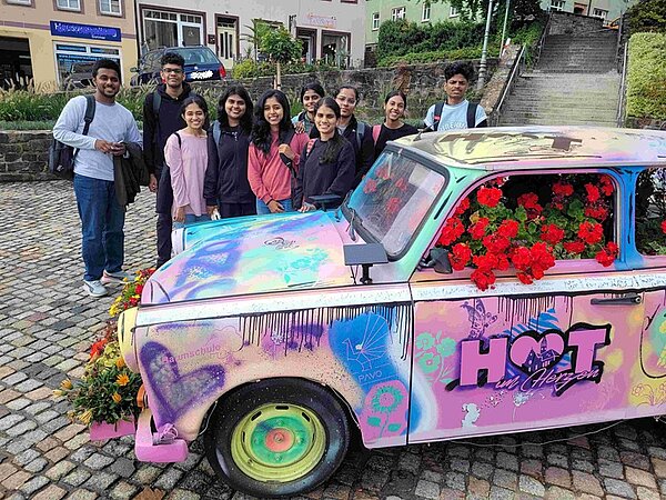 Gruppenfoto der neuen Auszubildenden aus Indien vor einem angesprayten Trabanten. 