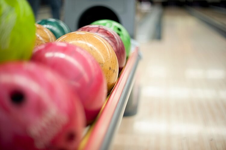 Eine Auswahl an bunten Bowlingkugeln, aufgereiht in einem Regal, bereit für ein Spiel auf der Bowlingbahn.