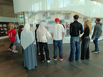 Die Schülerinnen und Schüler der Euro Akademie Leipzig stehen vor einer großen Vitrine mit Ausstellungsobjekten im Buch- und Schriftenmuseums in Leipzig.